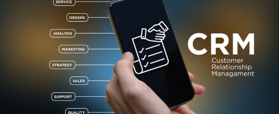 A person's hand holding a smartphone with the letters CRM displayed on the screen. The image highlights the benefits of using a CRM system, such as improved customer relationship management, increased sales and efficiency, and enhanced data analysis capabilities.